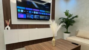 Una sala de estar moderna con un televisor de pantalla plana montado en la pared, una mesa de centro de madera, una planta en maceta y un sofá.