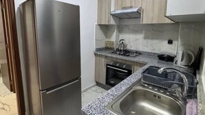 Una cocina compacta con un refrigerador de acero inoxidable, un horno empotrado, una estufa a gas y un lavabo con escurreplatos.