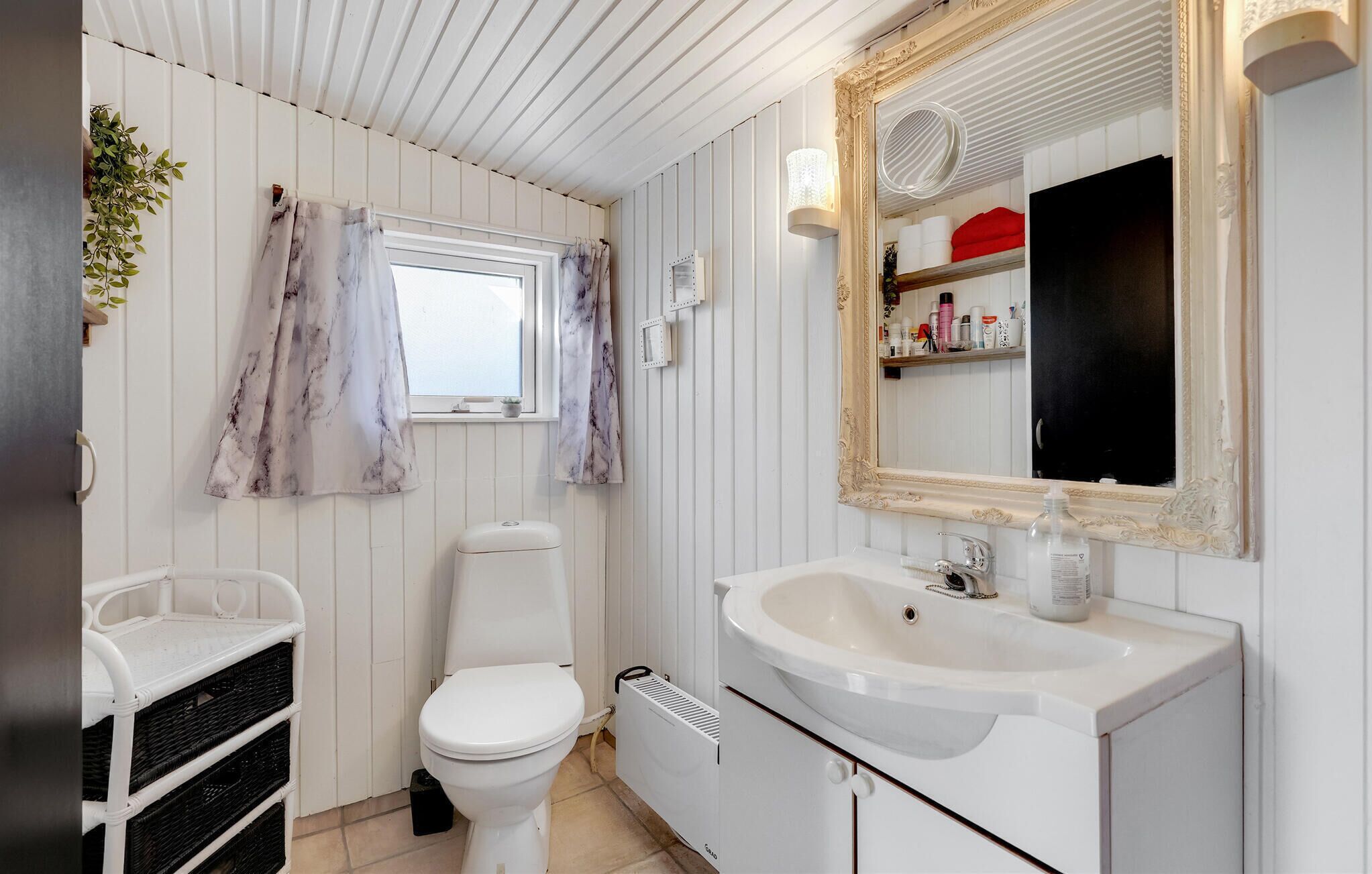 A bathroom with a white toilet, a sink with a mirror, and a window with curtains.