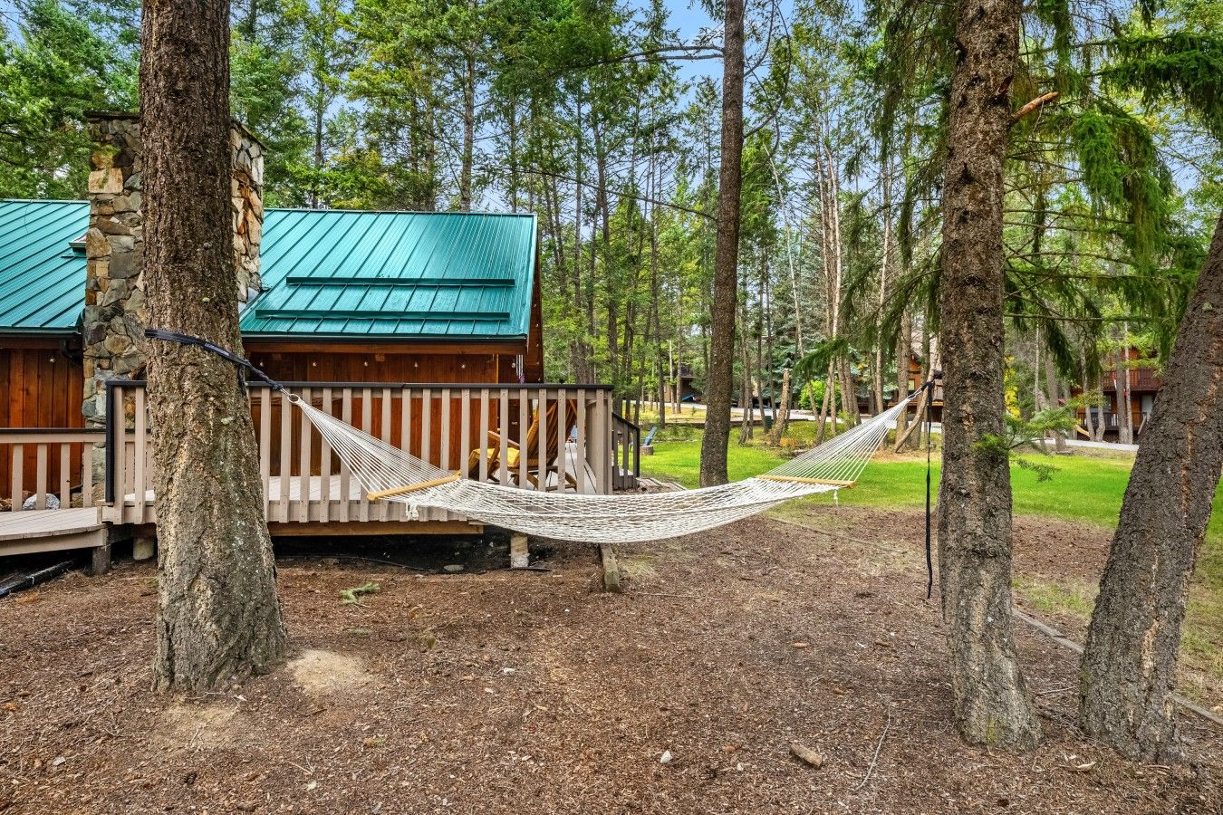 A wooden cabin with a green roof, surrounded by trees, and a hammock between two trees.