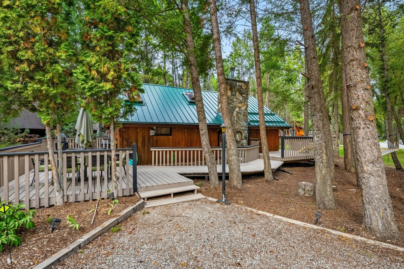 A cabin with a stone foundation and a metal roof, surrounded by trees and a wooden deck.