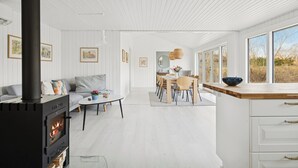 Un interior modern amb una estufa de llenya, una zona de menjador i grans finestres.