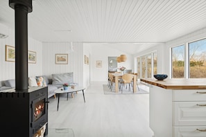 A modern interior with a wood-burning stove, a dining area, and large windows. - Bright holiday home with sunny terrace (Væggerløse)
