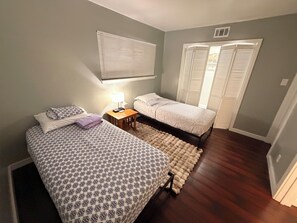 A bedroom with two beds, a nightstand, a lamp, a window with blinds, and a door with a closet. - Enjoyable 2 Story, 2-bedroom condo with AC Near Galleria HTX (Houston)