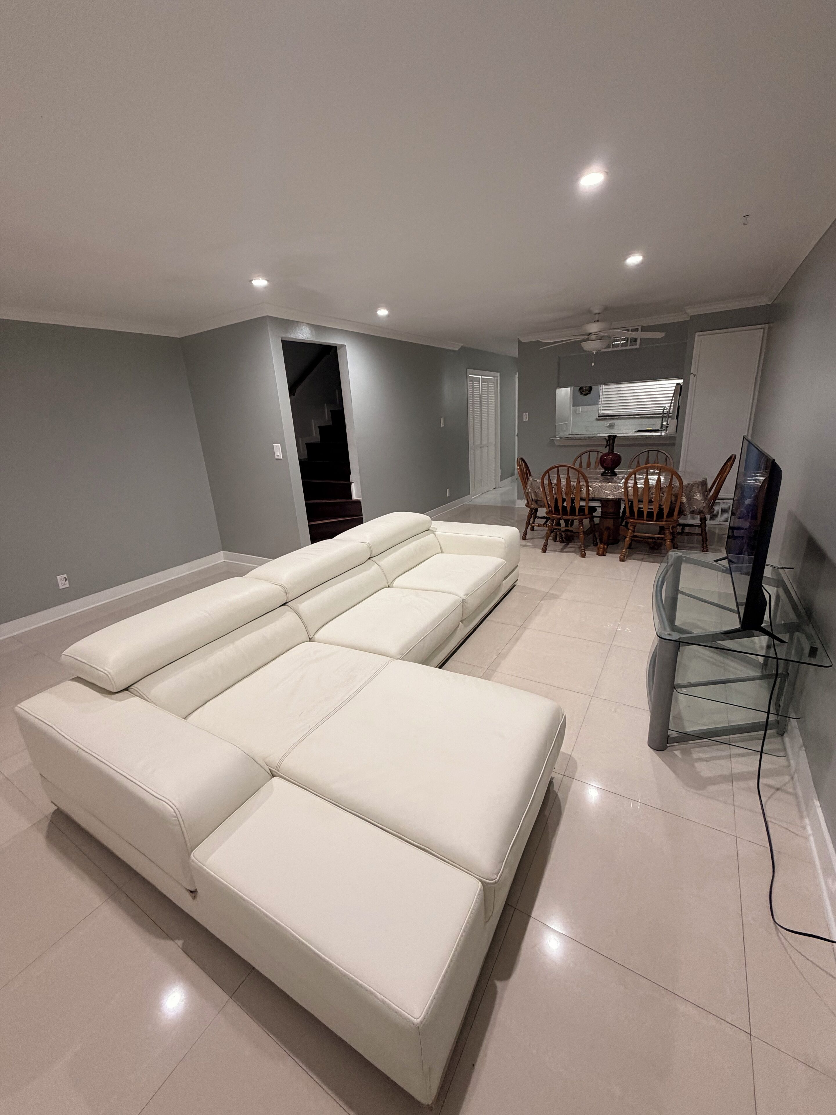Un vaste espace de vie comprenant un grand canapé d’angle blanc, une table à manger avec des chaises et un téléviseur posé sur un meuble en verre.