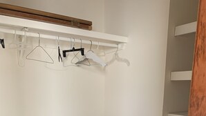 Um armário com prateleiras, um cabideiro de madeira e uma cesta de roupa.