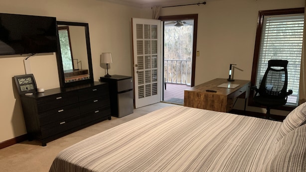 Quarto com cama, penteadeira, escrivaninha, cadeira, espelho e porta de vidro corria para varanda.