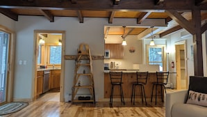 Un'ampia cucina con travi in legno, un'isola centrale con sgabelli da bar e una scaffalatura a scala con oggetti decorativi.