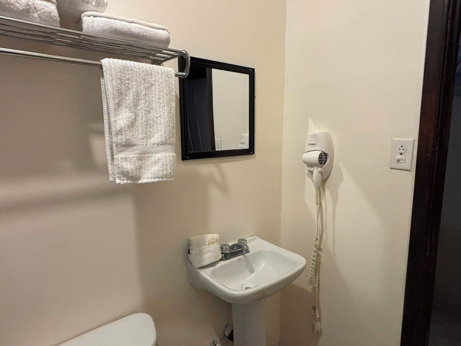 A bathroom with a white sink, a hair dryer, and a towel rack with a towel.