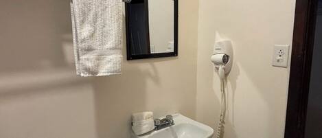 A bathroom with a white sink, a hair dryer, and a towel rack with a towel.