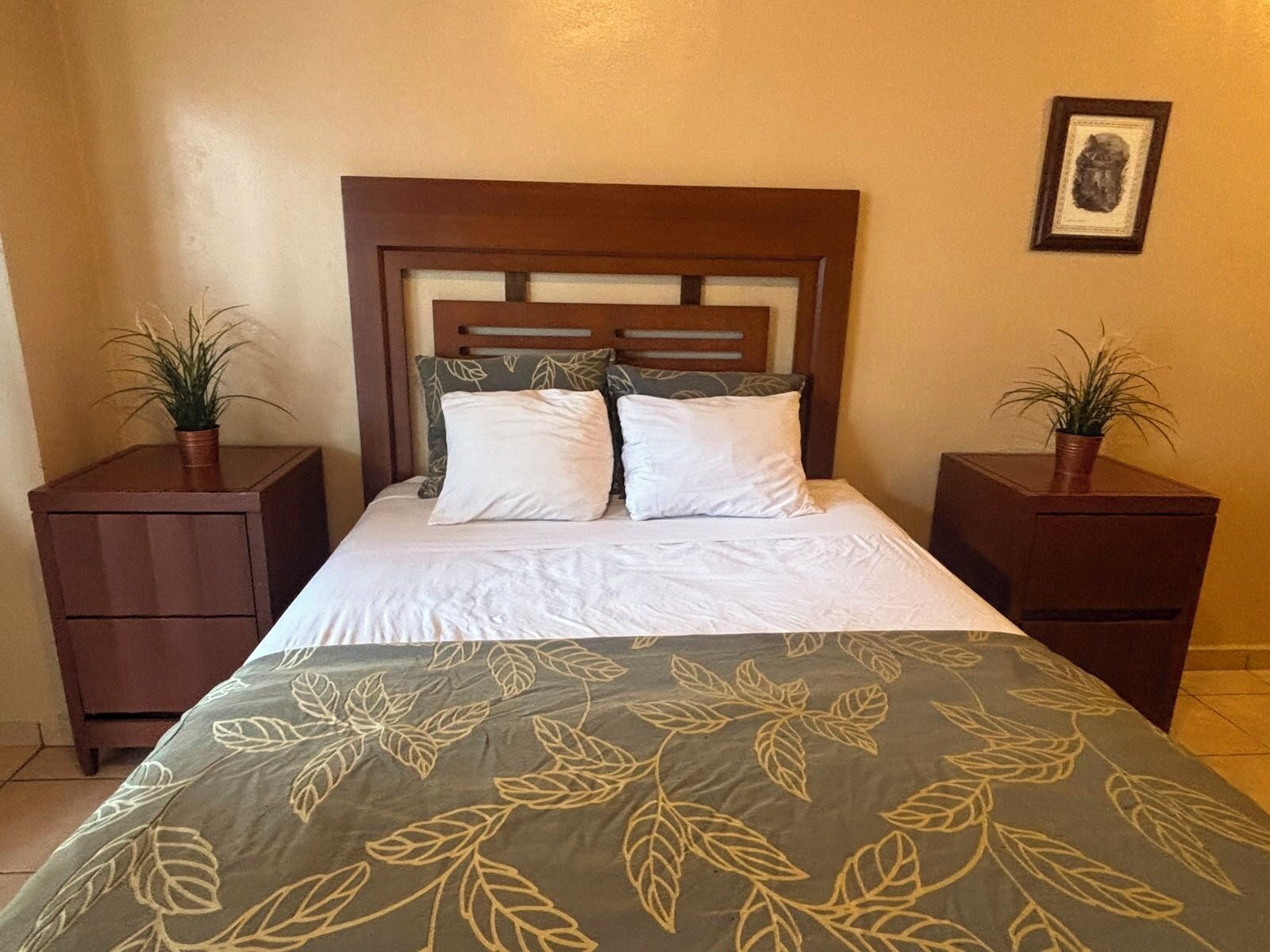 A hotel room with a bed, two nightstands, and two potted plants.