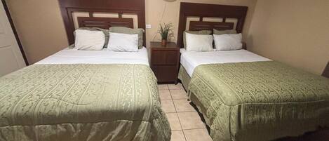A hotel room with two beds, a nightstand, a wall fan, and a potted plant.