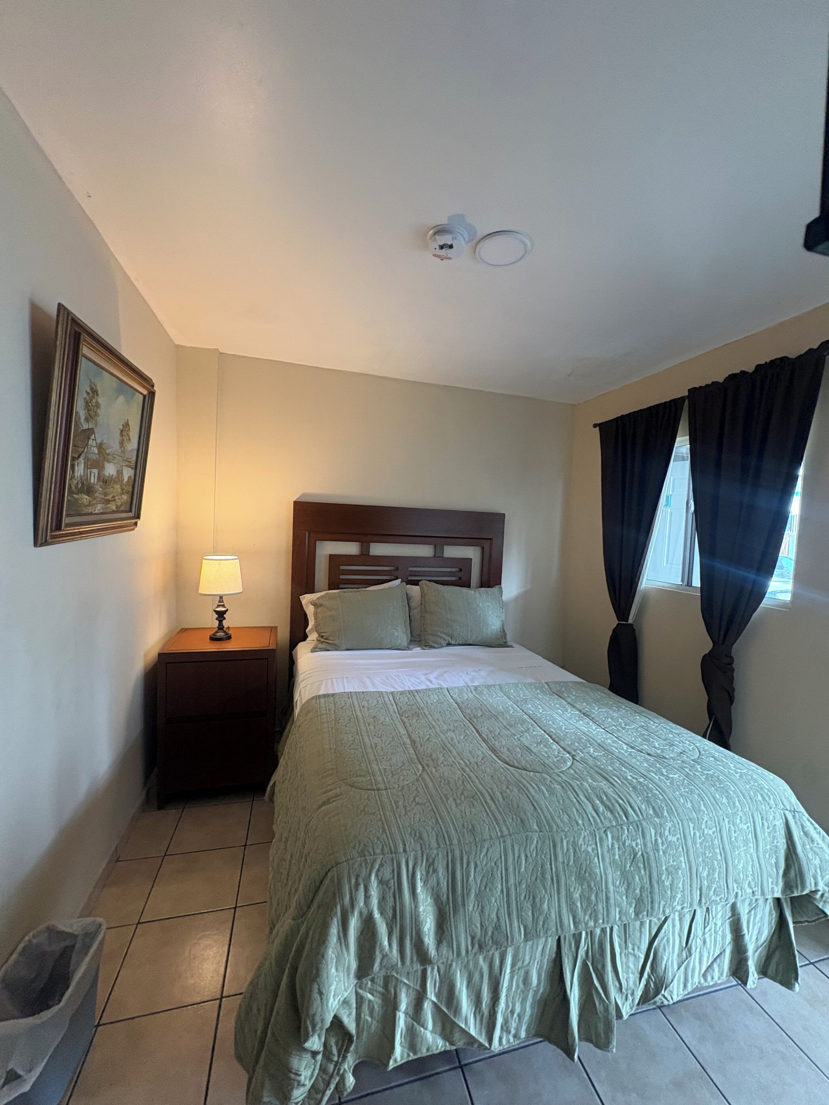 Un dormitorio con cama, mesita de noche, lámpara y un cuadro en la pared.