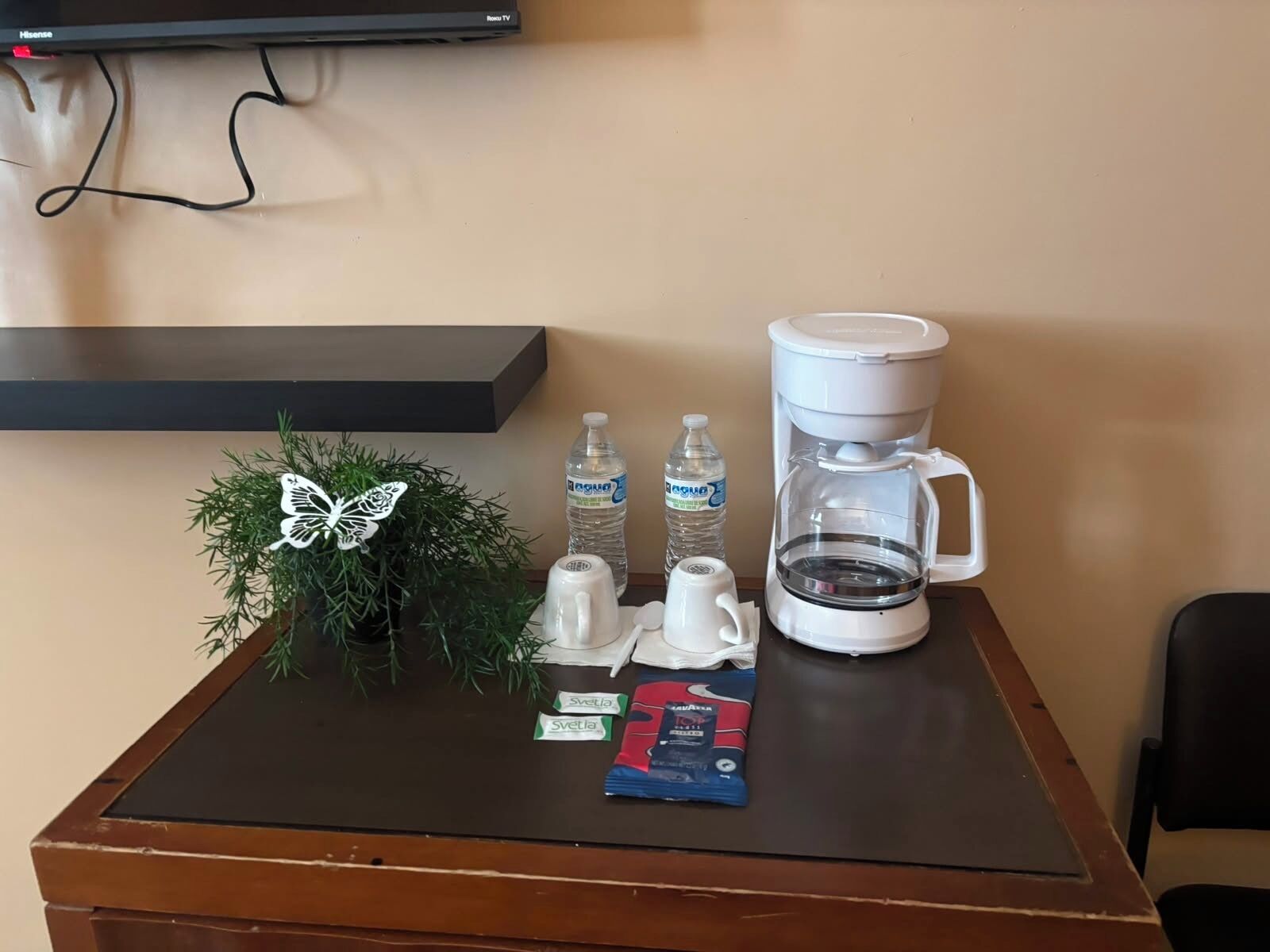 Una mesa con cafetera, botellas de agua, tetera, adorno de mariposa y un paquete de Svelia.