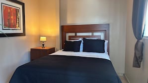 A hotel room with a bed, a nightstand, a lamp, a framed picture on the wall, and a window with curtains. - Motel del Bosque (Tijuana)