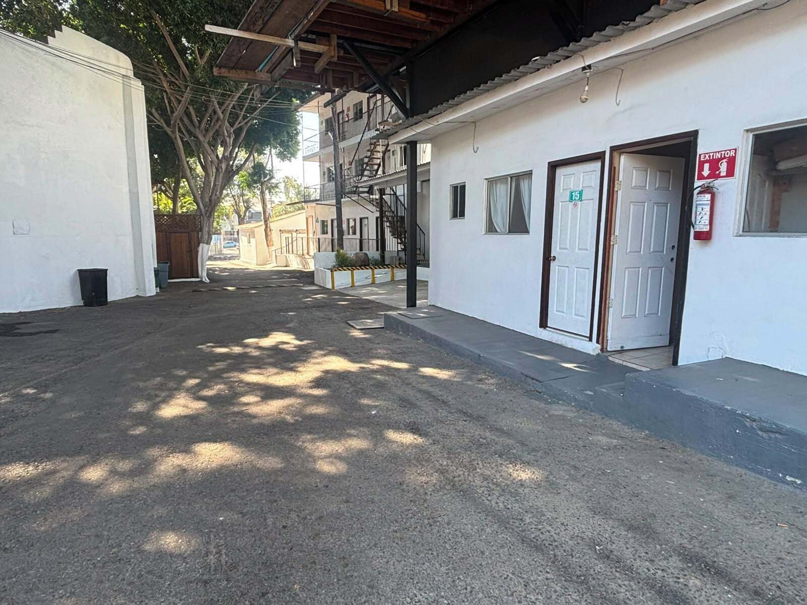 Une rue tranquille avec un bâtiment blanc, un panneau indiquant la présence d’un extincteur et une porte portant le numéro 15.