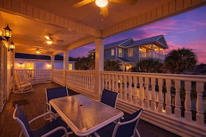 A covered outdoor deck with a table and chairs, a railing, and a view of a house in the background. - North Myrtle Beach - Sleeps 14 - Pool & Ping Pong (North Myrtle Beach)