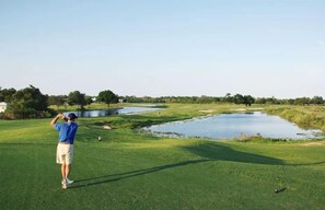 Ein Golfplatz mit Teich, Bäumen und blauem Himmel.
