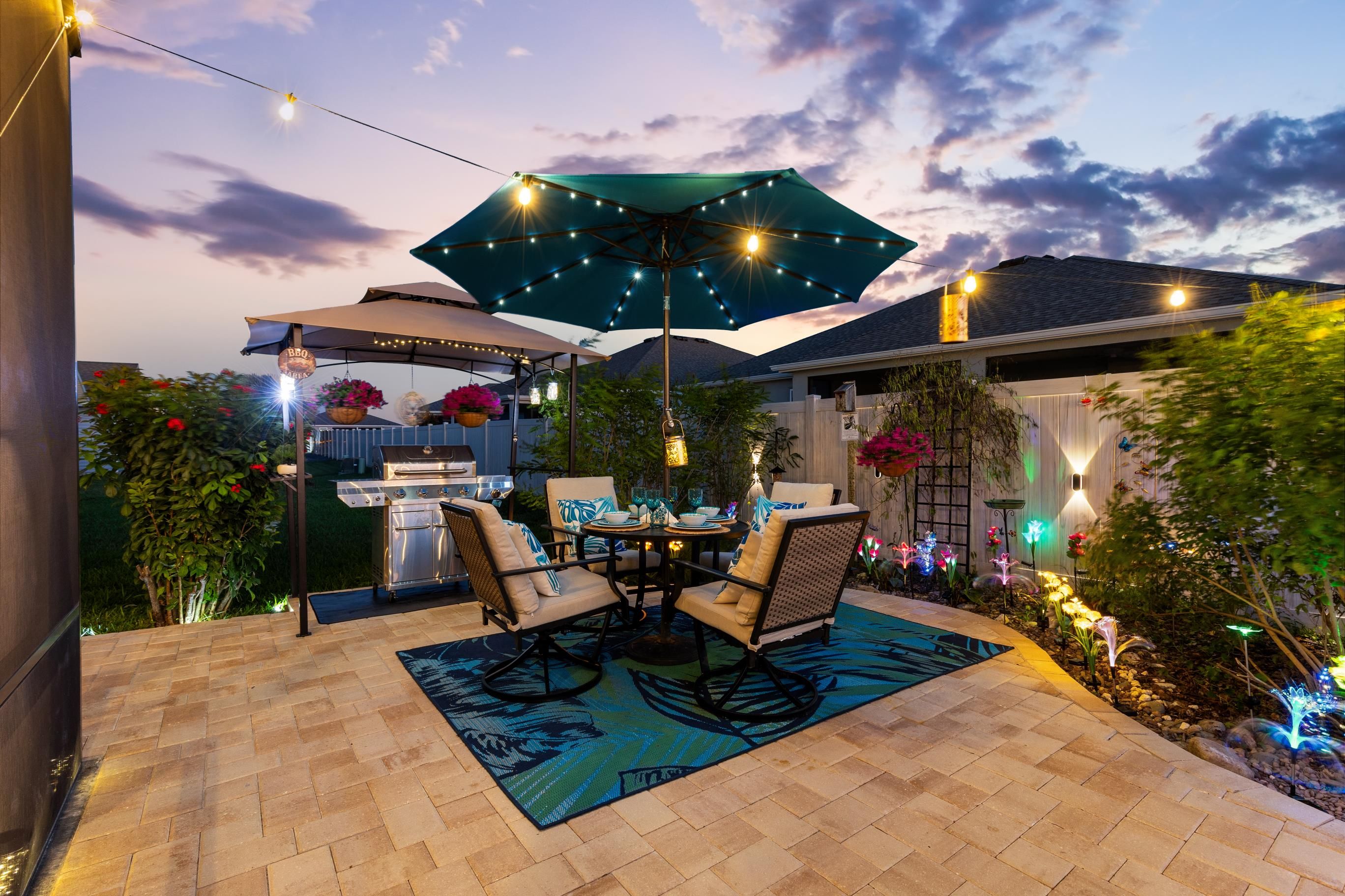 An outdoor patio with a grill, seating, and string lights.