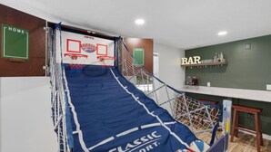 Un terrain de basket-ball installé à la maison, avec un panier, un coin bar et une pancarte indiquant « DOMICILE ».