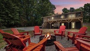 Une terrasse avec des fauteuils Adirondack rouges et un foyer au centre, entourée d’une zone de gravier avec des arbres en arrière-plan.