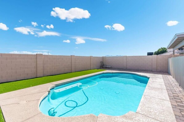 Une piscine rectangulaire dotée d’un jacuzzi intégré, entourée d’un mur de briques et d’une pelouse.