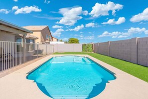 A rectangular swimming pool with a clear blue water surface, surrounded by a white fence and a green lawn. - Sunny 4BR Getaway w/ Private Pool (Goodyear)
