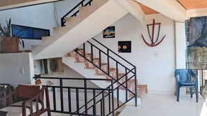 A spacious living area with a staircase, a blue plastic chair, and a potted plant. - Hotel Volga (Puerto Lopez)