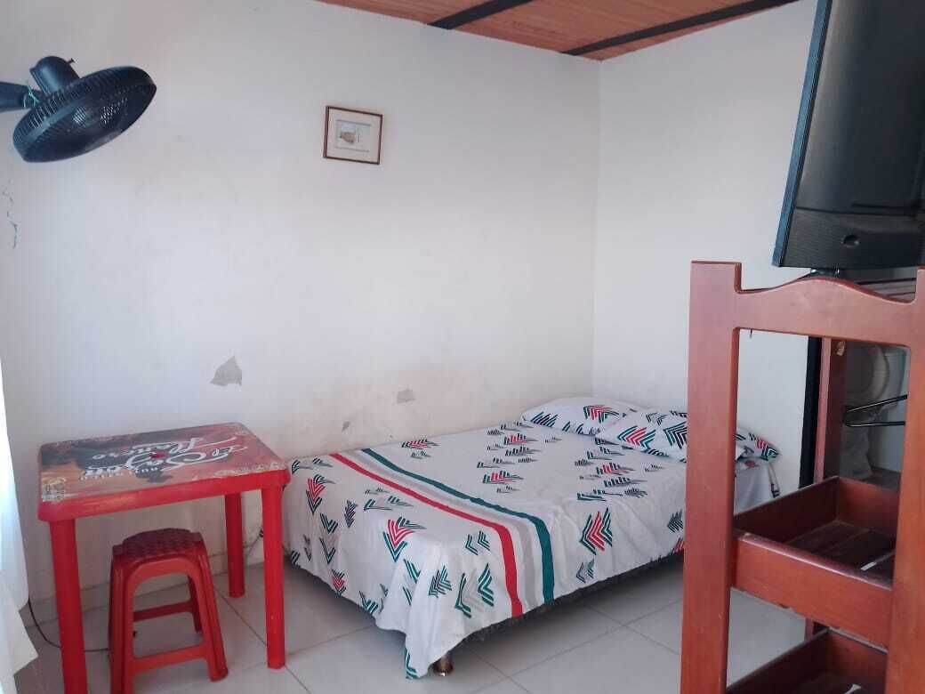 Una habitación pequeña con una cama individual, un escritorio, una silla, un televisor y un ventilador de techo.