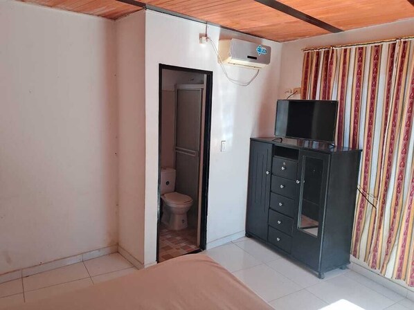 A bedroom with a bed, a wardrobe, a television, and a bathroom visible through an open door.