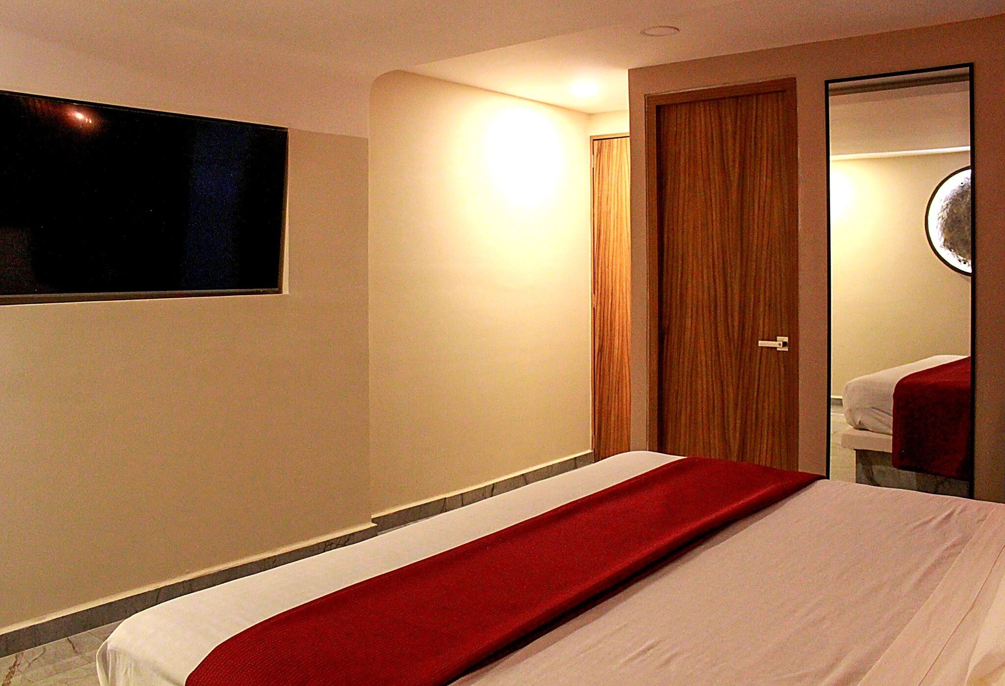A hotel room with a bed, a TV mounted on the wall, a door, and a mirror.