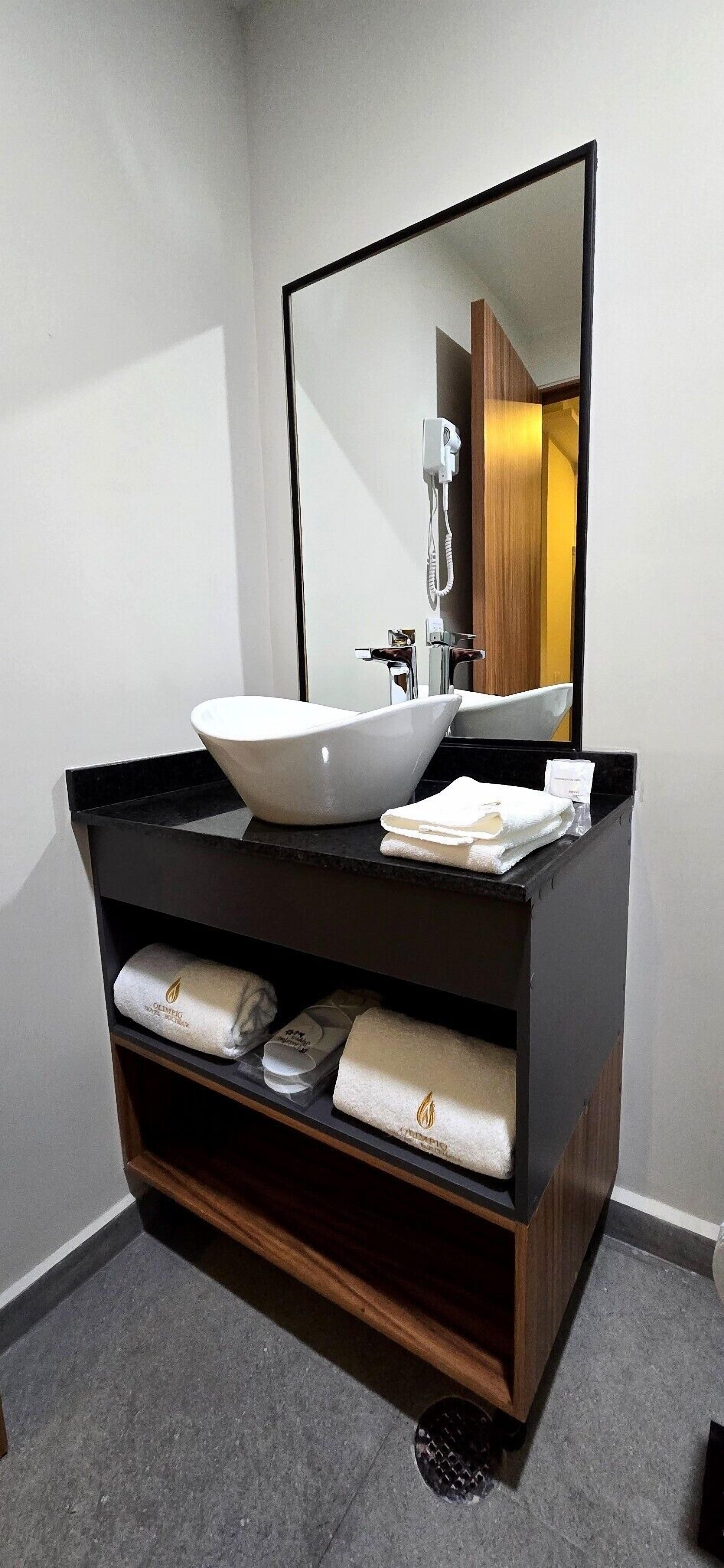 Un baño moderno con un espejo grande, un lavabo blanco tipo recipiente y un mueble de tocador de madera oscura.