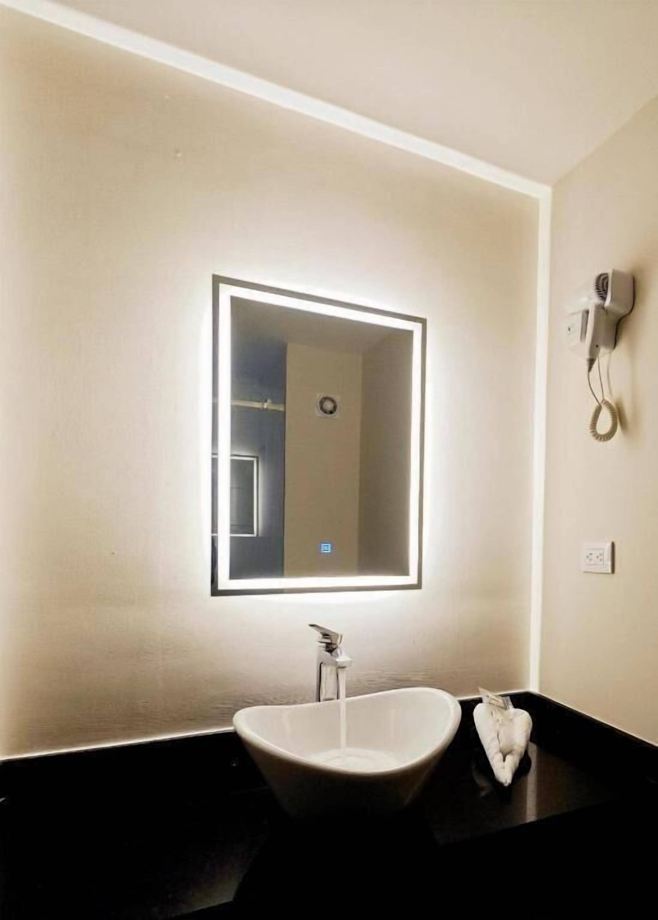 A bathroom with a white sink, a large mirror with a light, and a hairdryer on the wall.