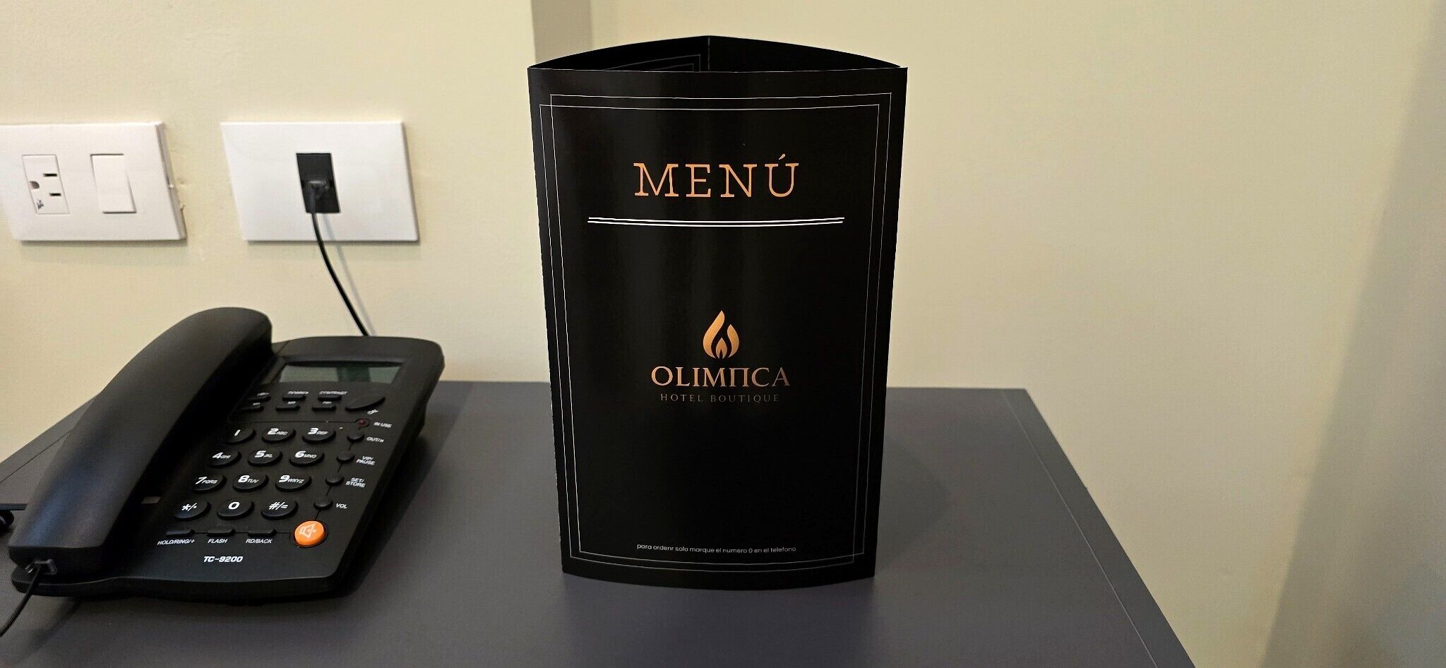 Musta puhelin ja musta teline, jossa on hotellin menulista. Telineessä lukee: »OLIMPIKA HOTEL BOUTIQUE».