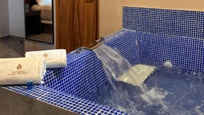 Un espace spa comprenant une baignoire carrelée de bleu, des serviettes et une porte en bois.