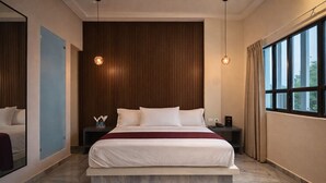 Une chambre d’hôtel moderne avec un grand lit, un mur lambrissé en bois, deux lampes suspendues, une table de chevet et une fenêtre avec des rideaux.