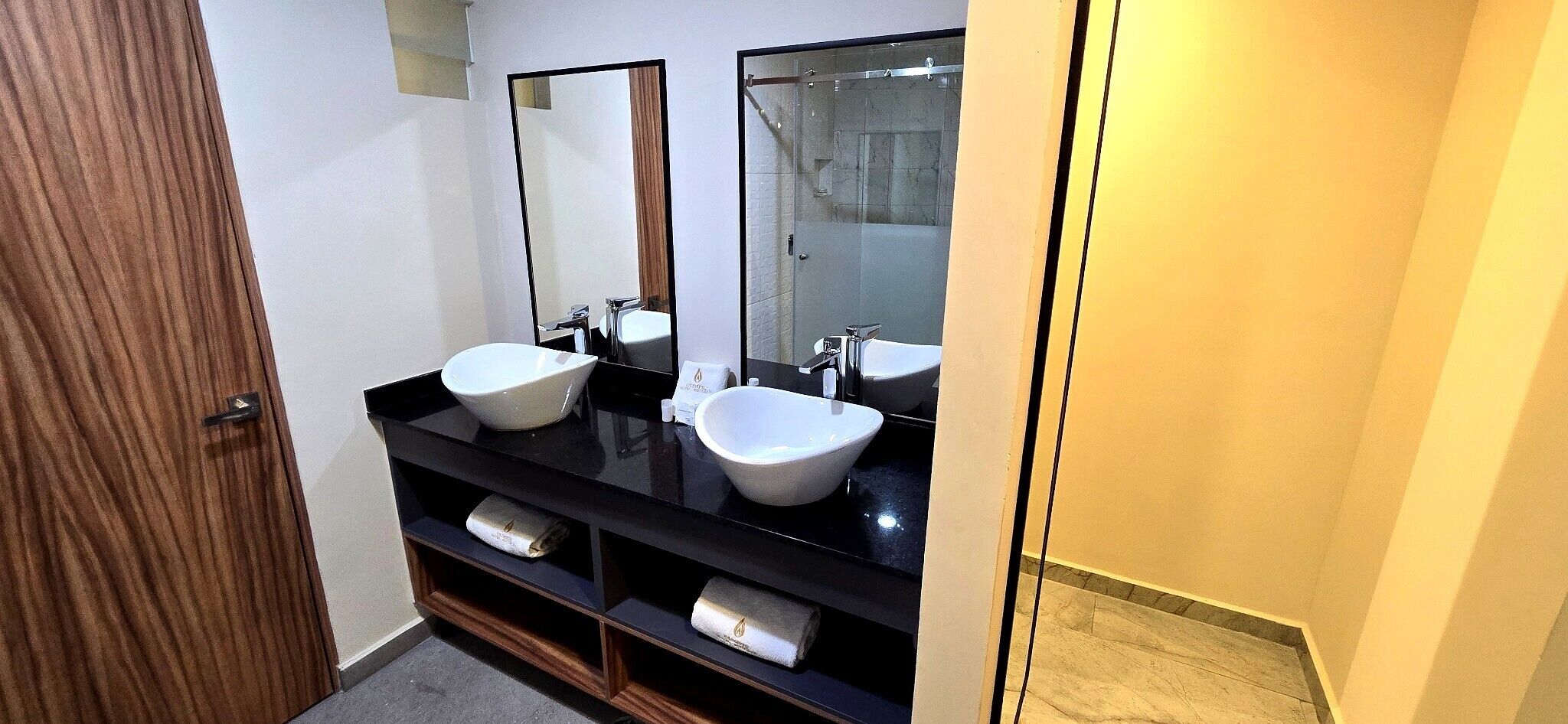 Un baño con dos lavamanos blancos tipo recipiente, una encimera negra y una puerta de madera.