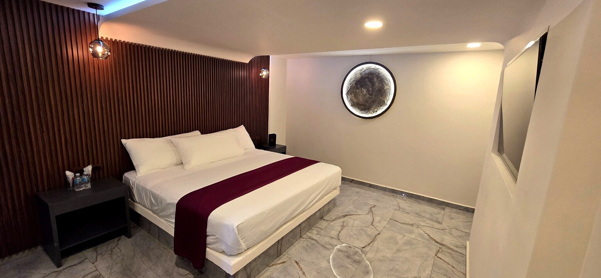 A hotel room with a bed, a nightstand, a circular wall decoration, and a marble floor.