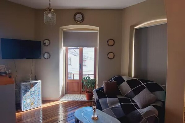 Una sala de estar con un sofá a cuadros, un televisor, una araña y una puerta que da al exterior.