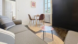 Een woonkamer met een bank, een klein tafeltje, twee stoelen, een vloerkleed en een groot zwart scherm.