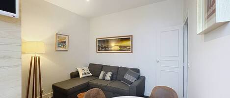 Een moderne woonkamer met een grijze bank, een ronde witte tafel en een vloerlamp.
