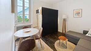 Een moderne woonkamer met een ronde eettafel, een bank, een vloerlamp en een groot zwart scherm.