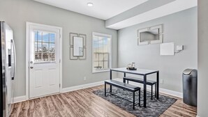 A modern living room with a gray wall, a white door, a dining table with benches, and a gray rug.