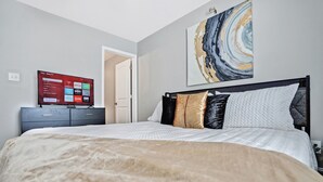 A bedroom with a bed, a TV on a dresser, and a door leading to another room.