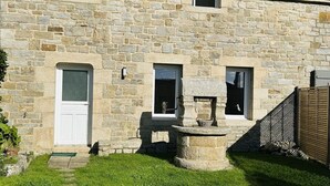 Ein Steinhaus mit einer Haustür, einem kleinen Fenster und einem Stebrunnen.