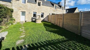 Ein Haus aus Stein mit einer Steintreppe, die zu einer Tür führt, ein kleiner Garten mit einem Steinfountain und ein Holzzaun.