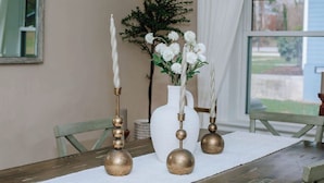 Una mesa de comedor con mantel blanco, tres candelabros decorativos y un jarrón con flores blancas.