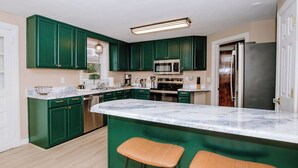 Una cocina moderna con gabinetes verdes, encimera de mármol y dos taburetes.