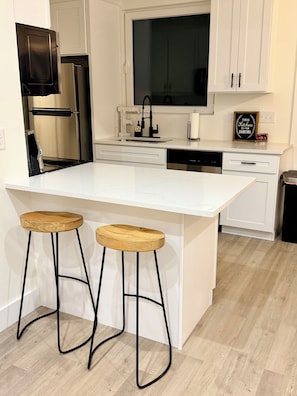Une cuisine moderne dotée d’un grand îlot central, de deux tabourets en bois, d’appareils électroménagers en acier inoxydable et de meubles de rangement blancs.