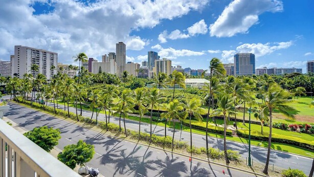 A cityscape with tall buildings, palm trees, and a clear sky. - In this cozy condominium located in Waikiki (Honolulu)